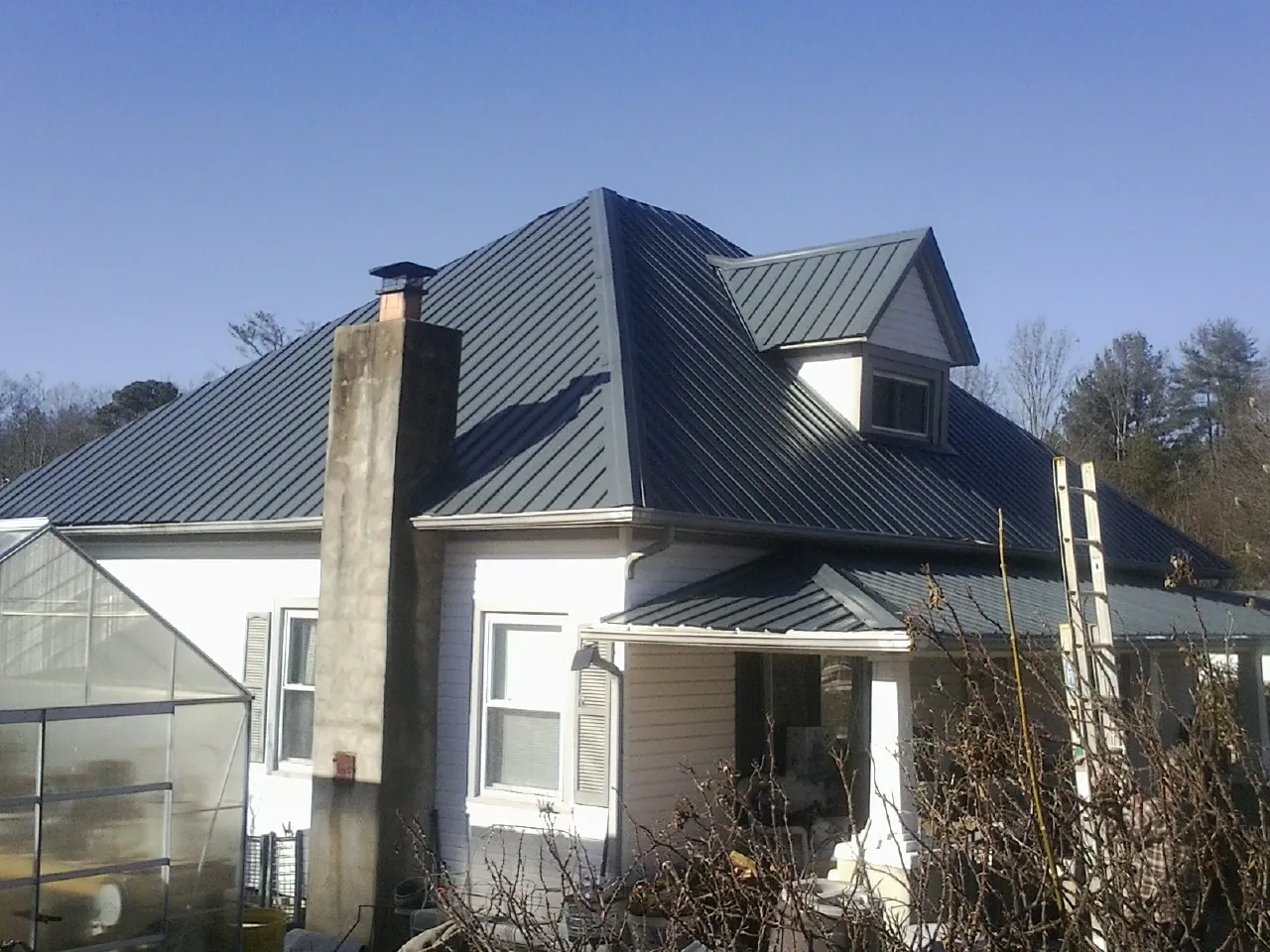 Dark blue standing seam metal roof on a white farmhouse with dormer — Slate & Tile Roof Repair by Roofing Brothers in Brush Creek