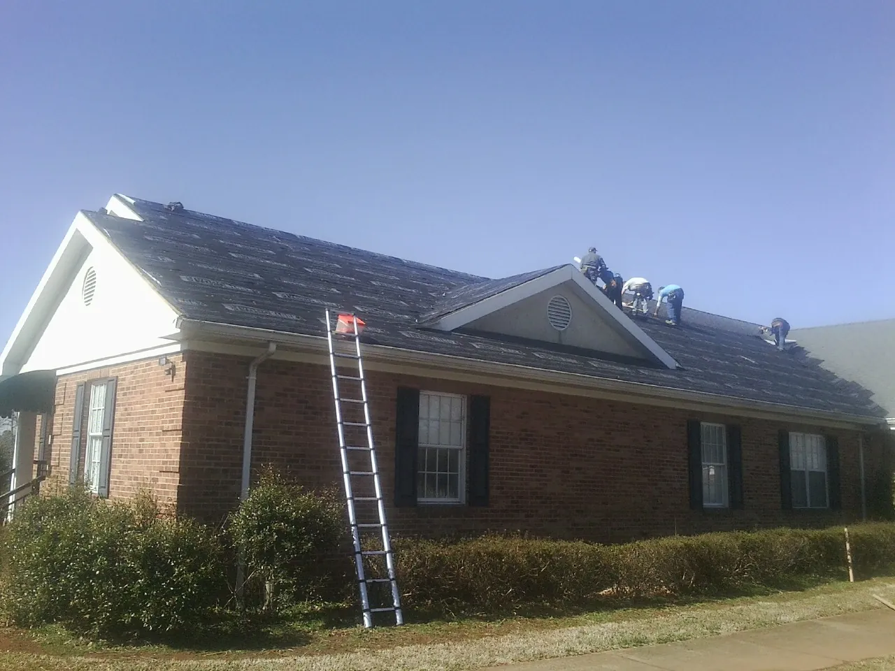 Crew tearing shingles off a brick ranch roof with a ladder set — Emergency Roof Repair work by our crew in Brush Creek