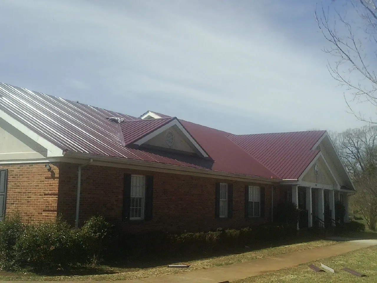 Red metal roof with gabled entries on a long brick building, from a Hail Damage Roof Repair job in Brush Creek