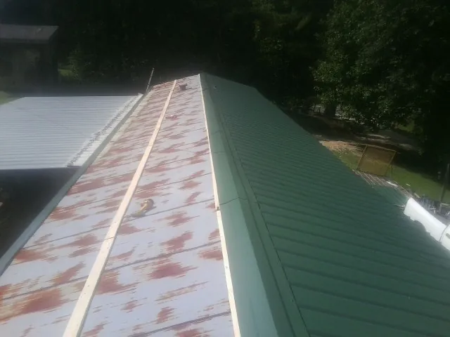 Old rusted panels beside newly installed green metal roofing — Wind Damage Roof Repair by Roofing Brothers in Brush Creek