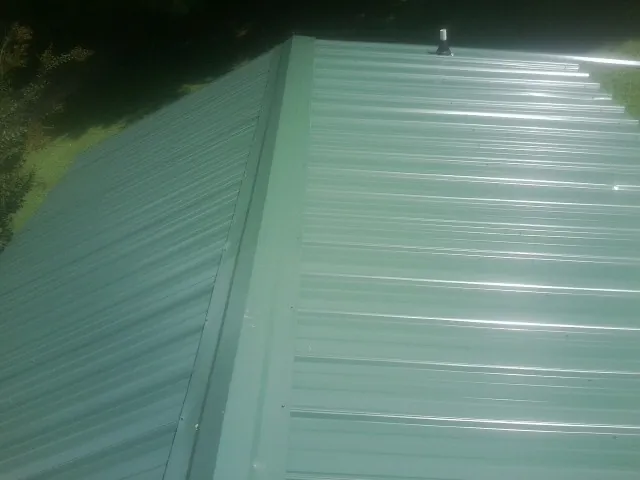 New green metal panels meeting at the ridge of a roof — Flat Roof Repair work by our crew in Brush Creek