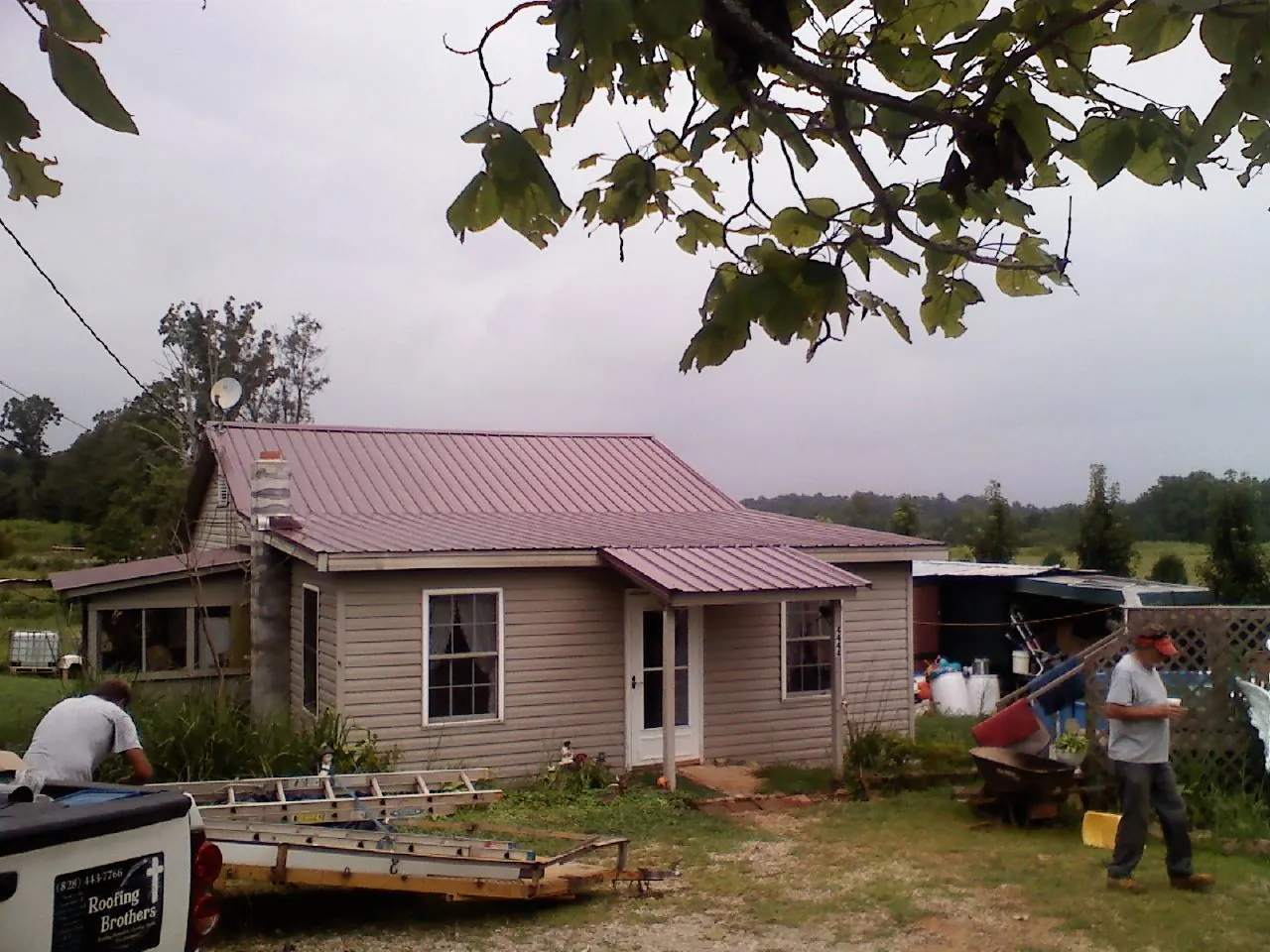 Crew finishing a mauve metal roof on a small farmhouse in Brush Creek