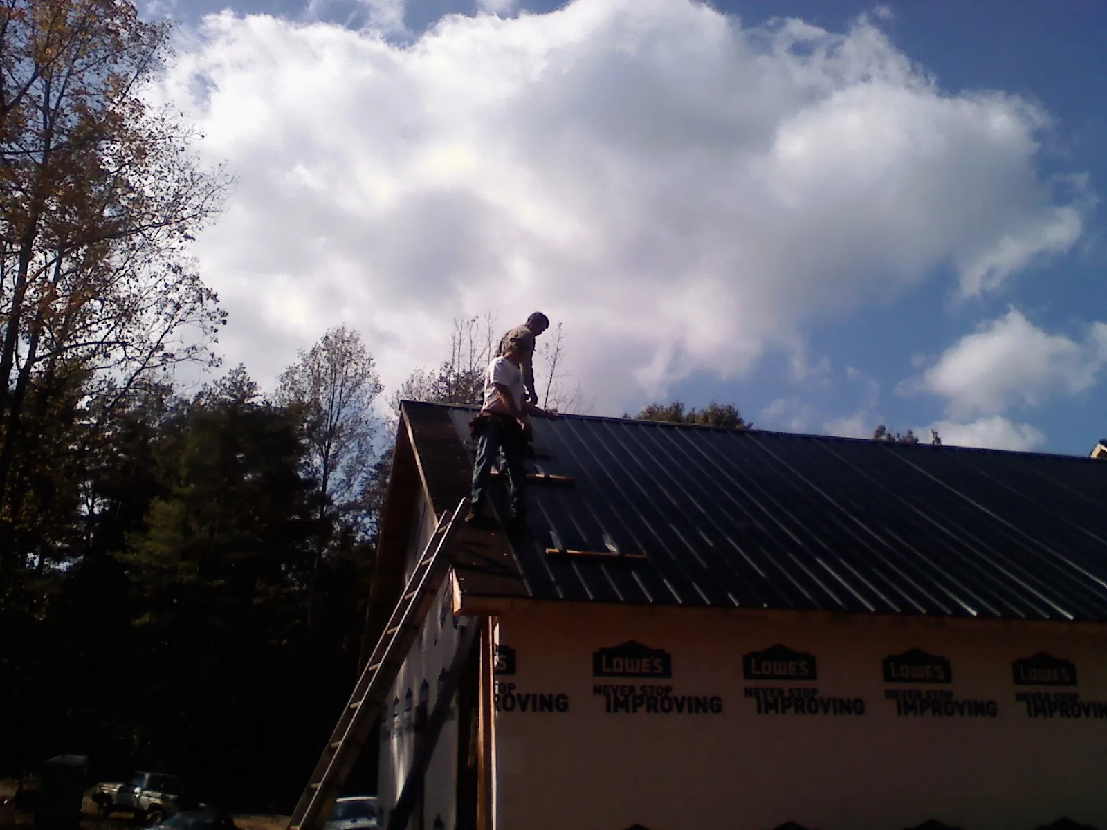 Roofer fastening dark metal panels high against a cloudy sky, from a Roof Inspection job in Brush Creek