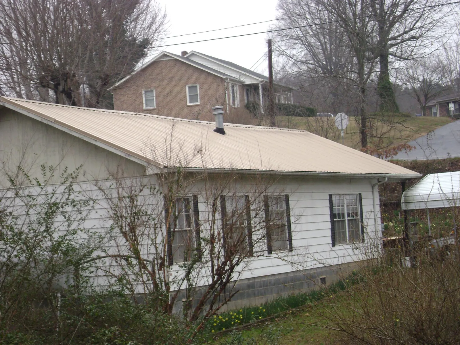 Tan metal roof on a white sided house set into a hillside — Commercial Roofing by Roofing Brothers in Brush Creek