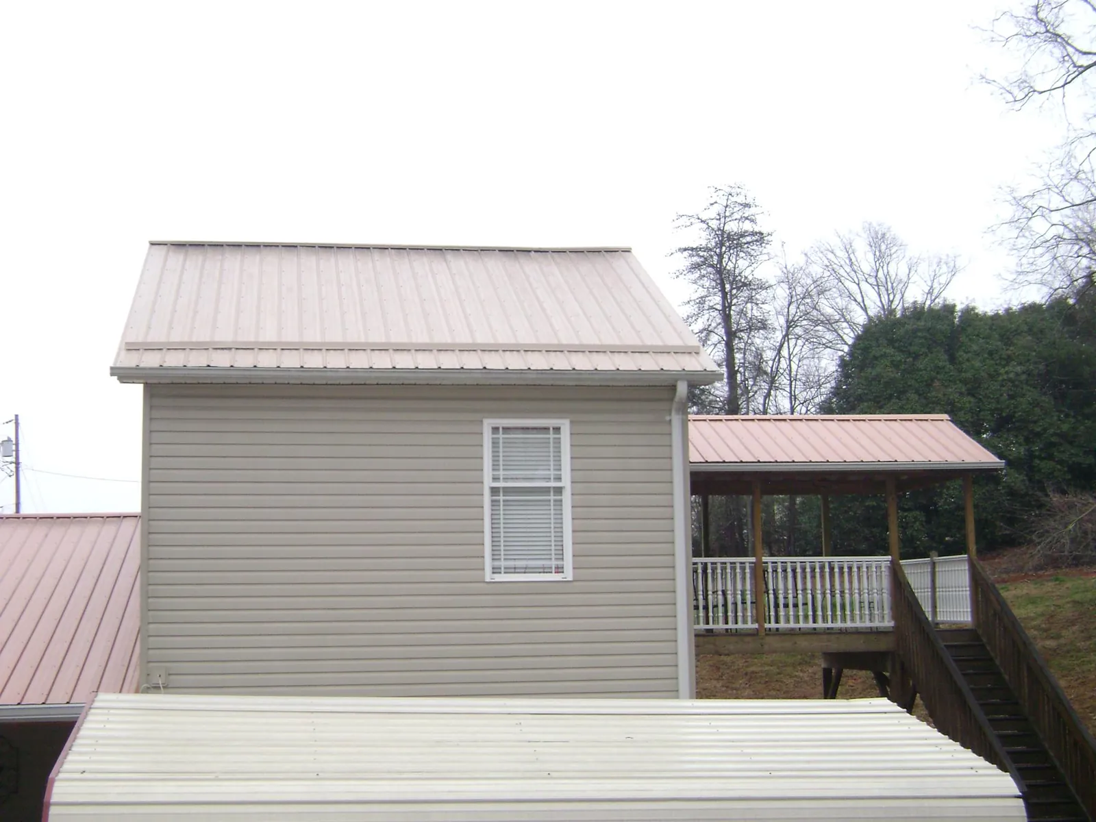 Tan metal roofs on a two story addition and attached porch, from a Roof Replacement job in Brush Creek